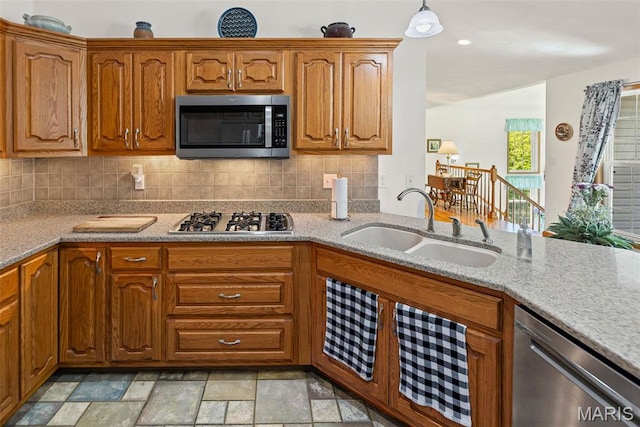kitchen featuring appliances with stainless steel finishes, a sink, light stone counters, and brown cabinets