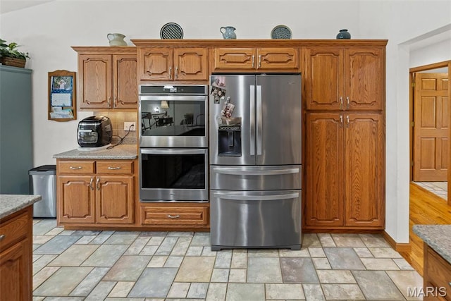 kitchen featuring stainless steel appliances, brown cabinets, stone finish floors, and light stone countertops