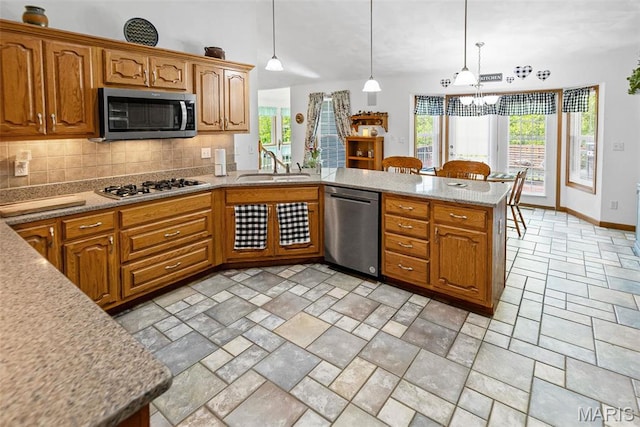 kitchen with appliances with stainless steel finishes, a sink, a peninsula, backsplash, and decorative light fixtures