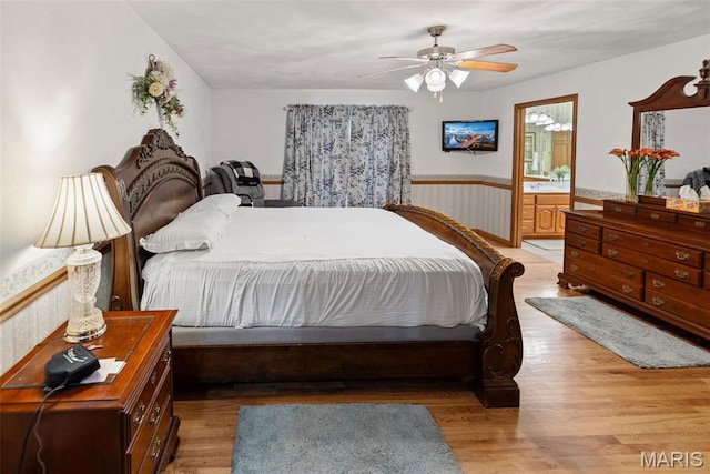 bedroom with wainscoting, light wood-style flooring, connected bathroom, and ceiling fan