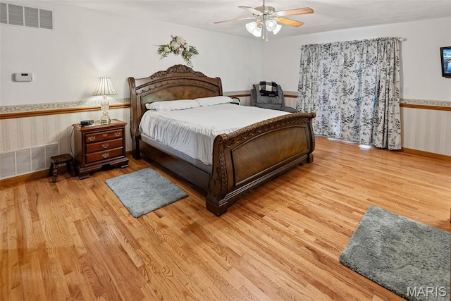 bedroom with light wood-type flooring, a ceiling fan, and wainscoting