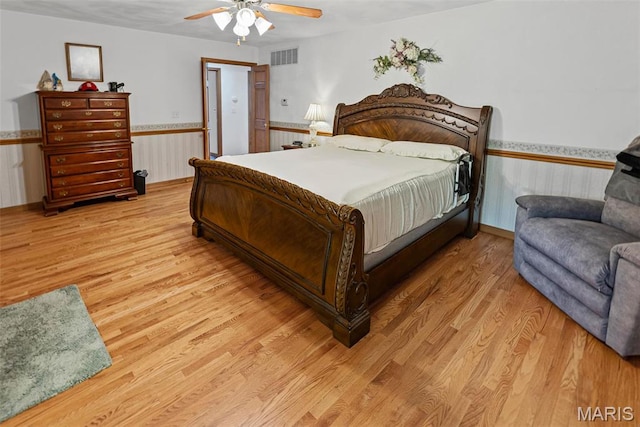 bedroom featuring light wood-style floors, a ceiling fan, and a wainscoted wall