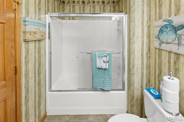 bathroom featuring wallpapered walls, toilet, bath / shower combo with glass door, and tile patterned flooring