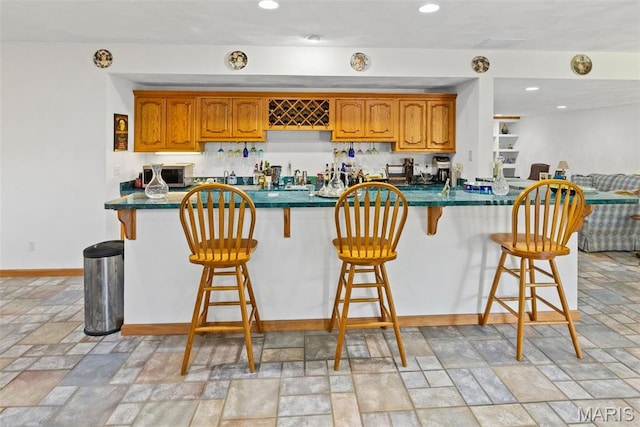kitchen with light stone finish floors, dark countertops, brown cabinetry, and recessed lighting
