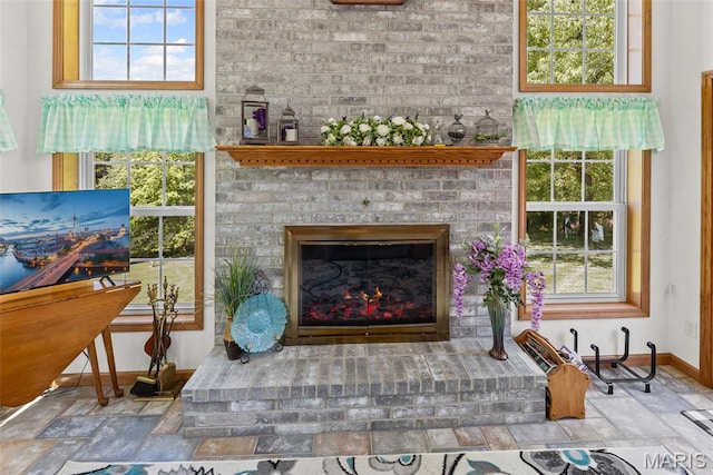 living room featuring baseboards, stone tile floors, a fireplace, and healthy amount of natural light