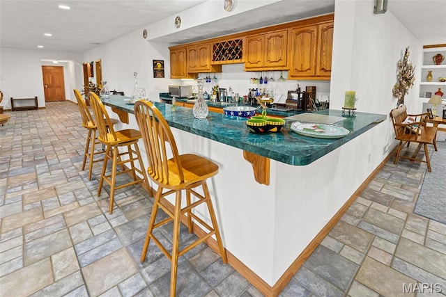 kitchen featuring dark countertops, stainless steel microwave, a peninsula, a kitchen breakfast bar, and brown cabinets