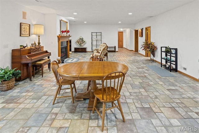 dining room featuring stone tile floors, baseboards, a glass covered fireplace, and recessed lighting