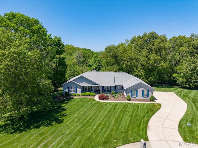 ranch-style house with a front lawn, concrete driveway, and a view of trees