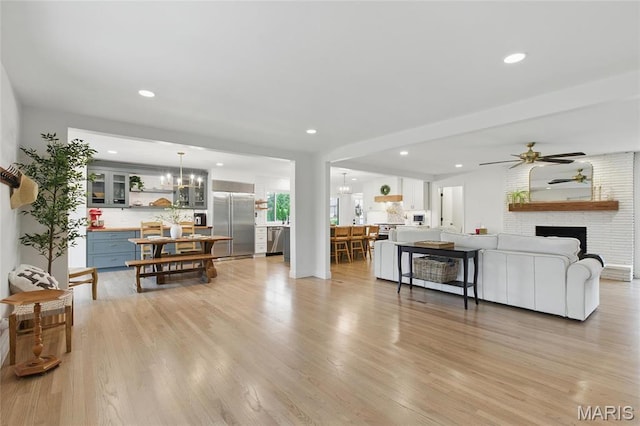 living room featuring light wood-type flooring, a chandelier, a ceiling fan, a fireplace, and recessed lighting