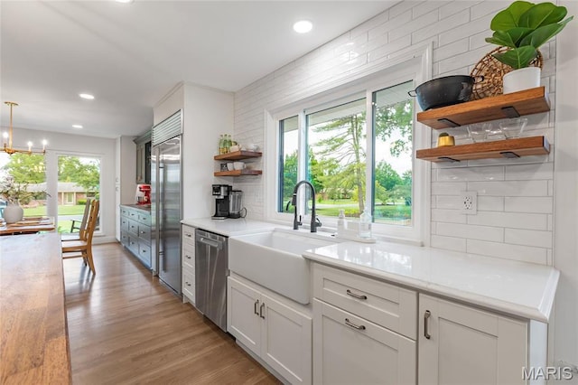 kitchen featuring open shelves, stainless steel appliances, a sink, light countertops, and a chandelier