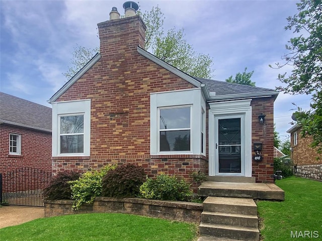 view of front of property with a chimney, a front lawn, brick siding, and roof with shingles