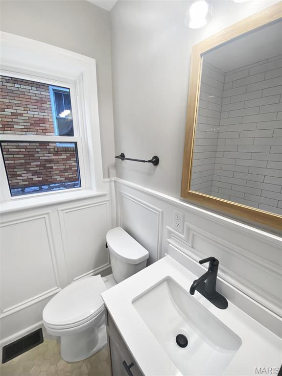 bathroom featuring a decorative wall, toilet, vanity, and a wainscoted wall