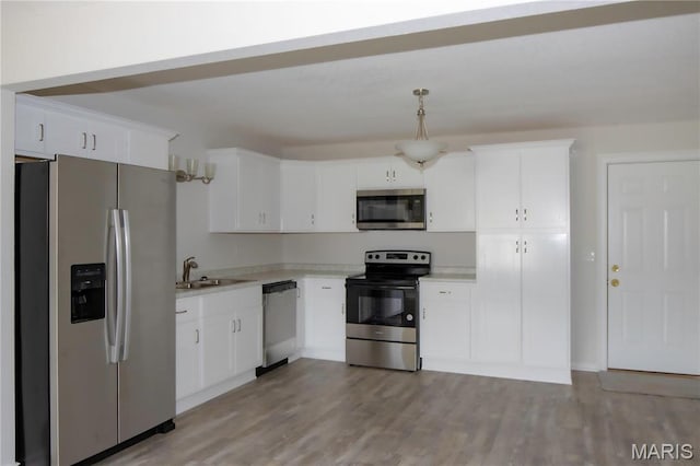 kitchen with appliances with stainless steel finishes, a sink, light countertops, white cabinetry, and light wood-style floors