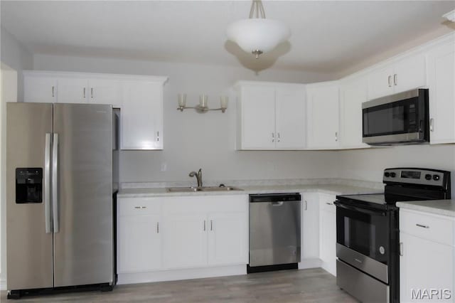 kitchen with stainless steel appliances, a sink, white cabinets, light countertops, and light wood-style floors