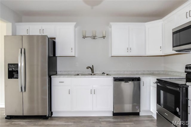 kitchen featuring appliances with stainless steel finishes, a sink, white cabinets, and light wood-style floors