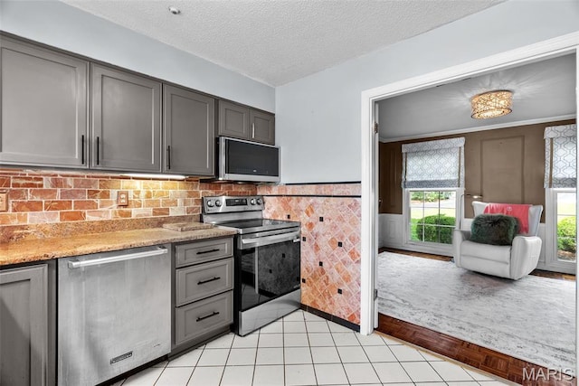 19 Sackston Woods Ln, Saint Louis, MO 63141 - kitchen featuring stainless steel appliances, gray cabinets, light tile patterned flooring, a wainscoted wall, and a textured ceiling