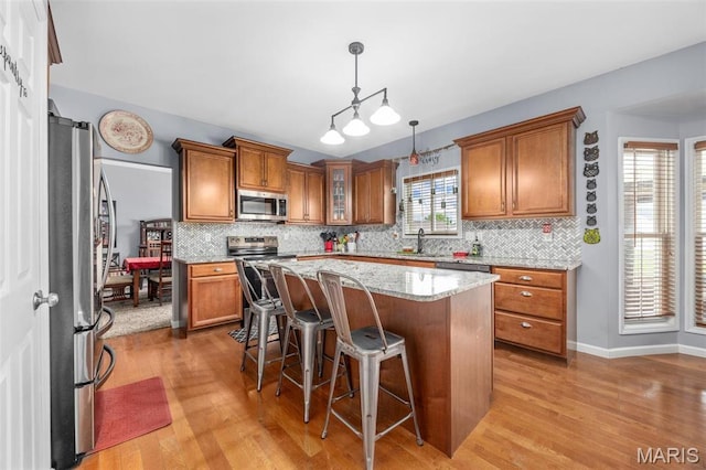 kitchen with appliances with stainless steel finishes, a sink, brown cabinetry, light wood-style floors, and decorative backsplash