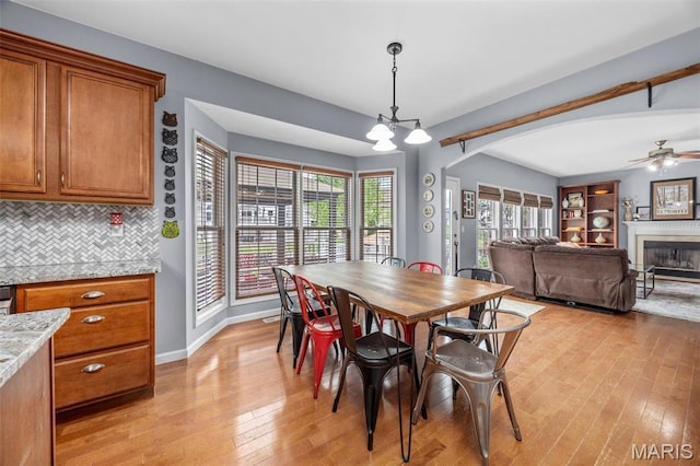 dining area with light wood-type flooring, a glass covered fireplace, a chandelier, baseboards, and arched walkways