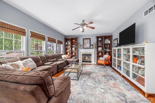 living area with a ceiling fan, wood finished floors, and a fireplace with flush hearth