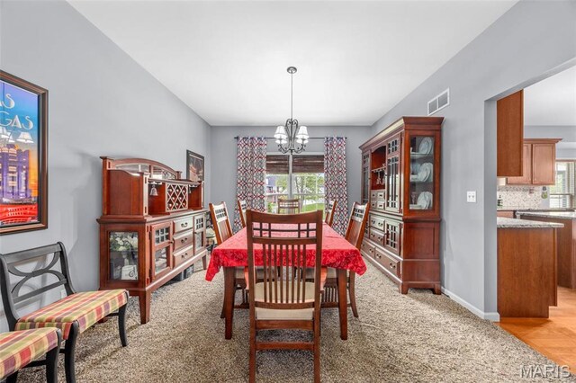 dining space featuring a chandelier, light colored carpet, and baseboards
