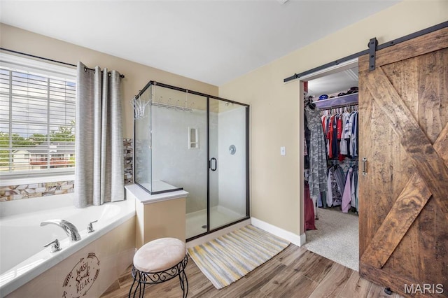 bathroom featuring wood finished floors, a bath, a stall shower, a walk in closet, and baseboards