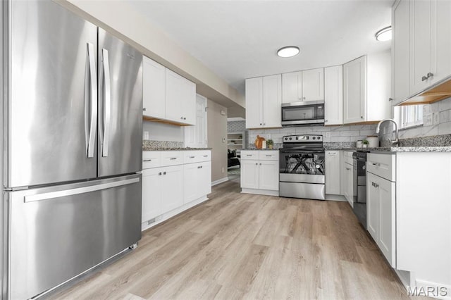 948 Barbara Ann Ln, Ellisville, MO 63021 - kitchen featuring stainless steel appliances, light wood-style floors, white cabinetry, decorative backsplash, and light stone countertops