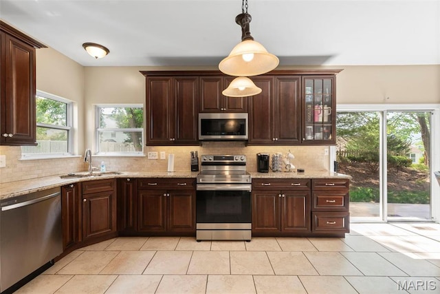 kitchen with appliances with stainless steel finishes, a sink, tasteful backsplash, and decorative light fixtures