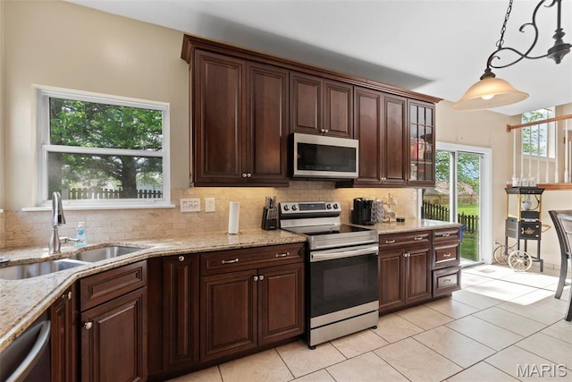 kitchen with appliances with stainless steel finishes, a sink, backsplash, decorative light fixtures, and light tile patterned floors