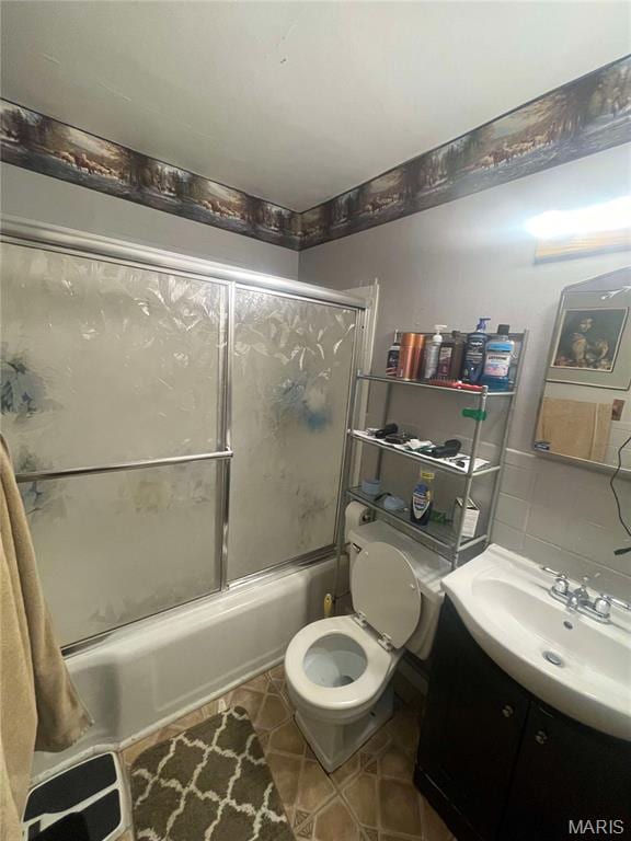 full bath featuring combined bath / shower with glass door, tile patterned flooring, vanity, and toilet
