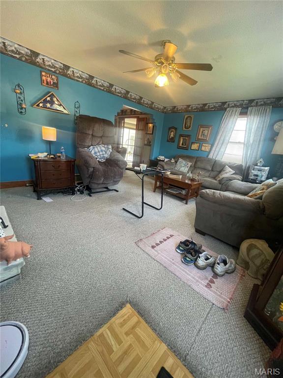 living area featuring ceiling fan, carpet flooring, baseboards, and a textured ceiling