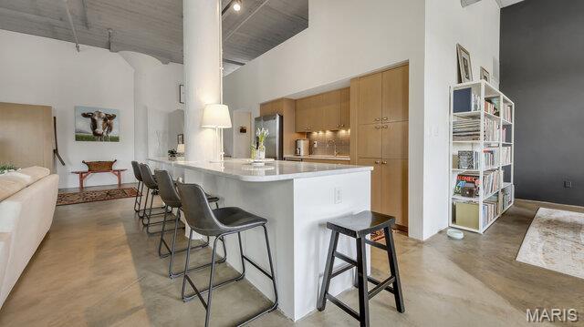 4100 Laclede Ave Unit 314, Saint Louis, MO 63108 - kitchen featuring a towering ceiling, freestanding refrigerator, a breakfast bar, finished concrete floors, and light countertops