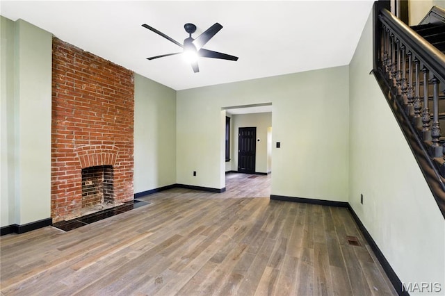 4402 Arco Ave, Saint Louis, MO 63110 - unfurnished living room featuring ceiling fan, wood finished floors, stairway, a brick fireplace, and baseboards