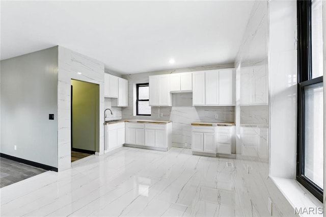 4402 Arco Ave, Saint Louis, MO 63110 - kitchen featuring white cabinets, a sink, backsplash, light marble finish floors, and baseboards