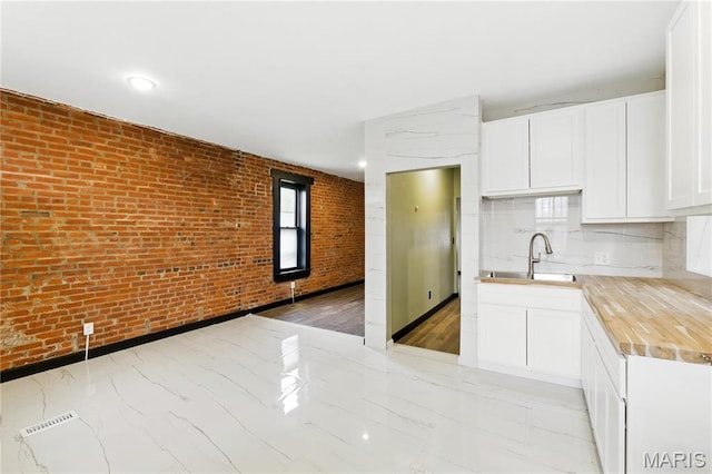 4402 Arco Ave, Saint Louis, MO 63110 - kitchen with a sink, brick wall, white cabinetry, and backsplash