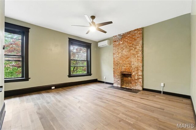 4402 Arco Ave, Saint Louis, MO 63110 - unfurnished living room featuring a wall mounted AC, ceiling fan, wood finished floors, a fireplace, and healthy amount of natural light
