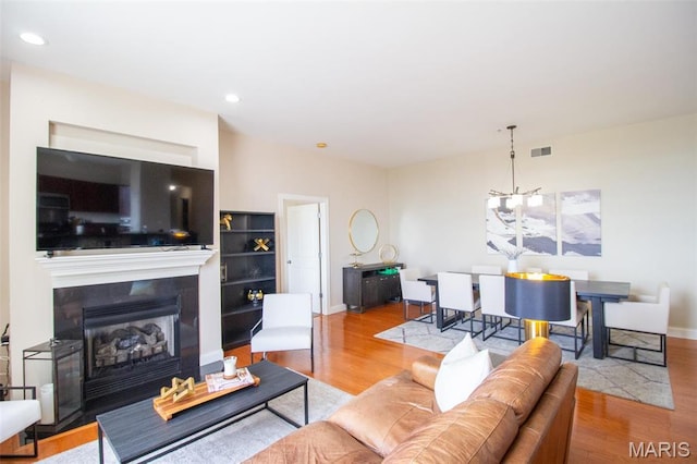 living room with wood finished floors, built in shelves, a fireplace with raised hearth, recessed lighting, and baseboards