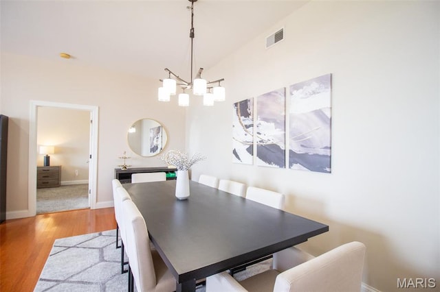 dining room featuring a chandelier, light wood finished floors, baseboards, and lofted ceiling
