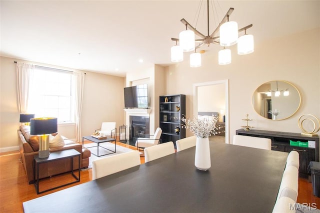 dining area with a fireplace with flush hearth, a chandelier, wood finished floors, and baseboards