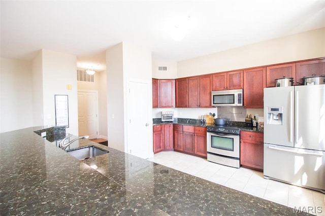 kitchen with stainless steel appliances, a sink, reddish brown cabinets, and dark stone countertops