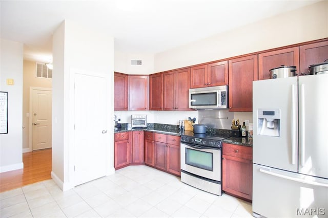 kitchen with stainless steel appliances, dark brown cabinets, dark stone counters, and light tile patterned flooring