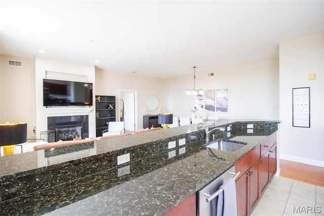 kitchen with a sink, dishwasher, a glass covered fireplace, light tile patterned floors, and open floor plan