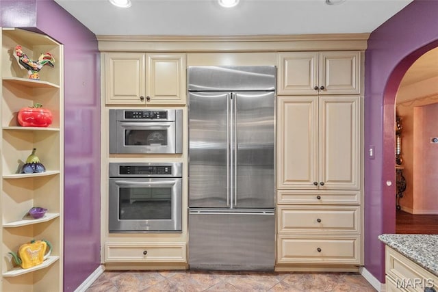 2048 Pontoon Rd, Granite City, IL 62040 - kitchen featuring appliances with stainless steel finishes, cream cabinetry, arched walkways, light stone counters, and built in features