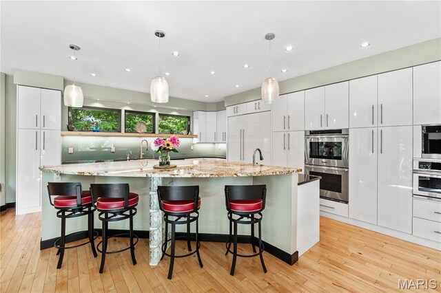 400 Gabriel Dr, Kirkwood, MO 63122 - kitchen with stainless steel double oven, white cabinets, light wood-type flooring, a large island with sink, and recessed lighting