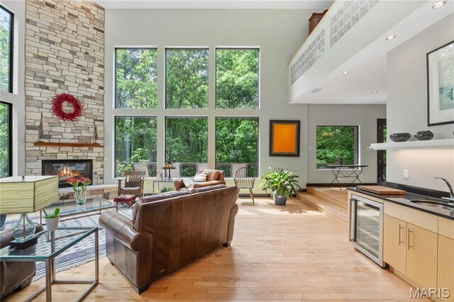 400 Gabriel Dr, Kirkwood, MO 63122 - living area with beverage cooler, a towering ceiling, healthy amount of natural light, light wood-type flooring, and a stone fireplace
