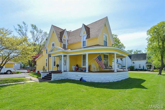 view of front of property with a front lawn, roof with shingles, and covered porch