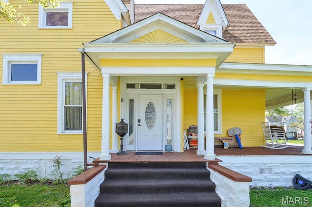 view of exterior entry with covered porch and a shingled roof