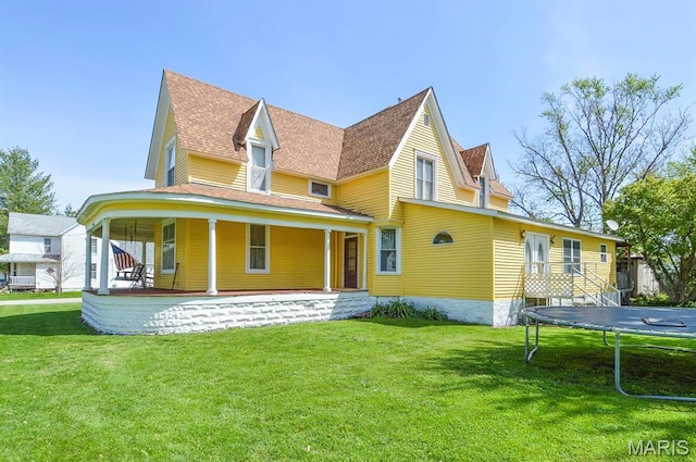 back of property featuring a trampoline, a yard, covered porch, and a shingled roof