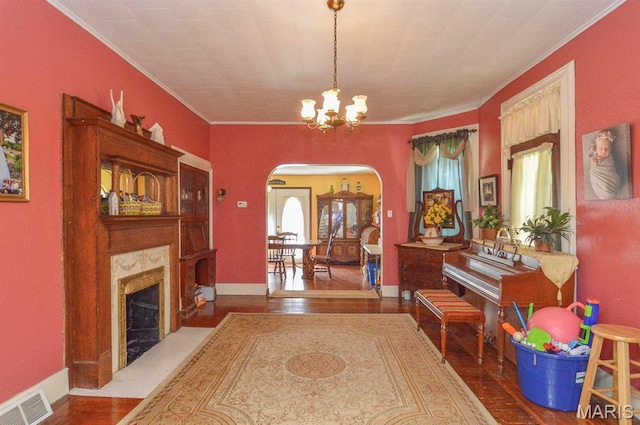 foyer featuring arched walkways, a chandelier, crown molding, wood finished floors, and a fireplace