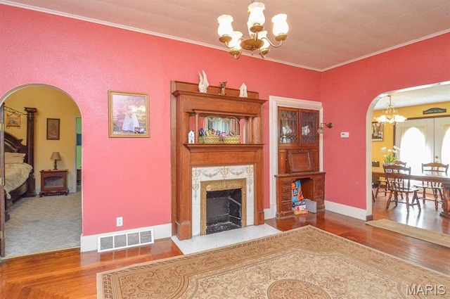 living room featuring arched walkways, a chandelier, a high end fireplace, wood finished floors, and crown molding
