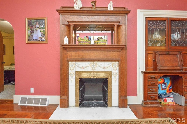 detailed view of wood finished floors, arched walkways, and a tiled fireplace